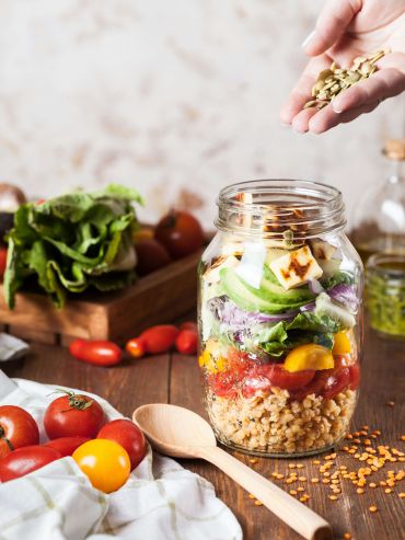 Hand adding seeds to jar salad representing gut microbiome and fiber for digestion